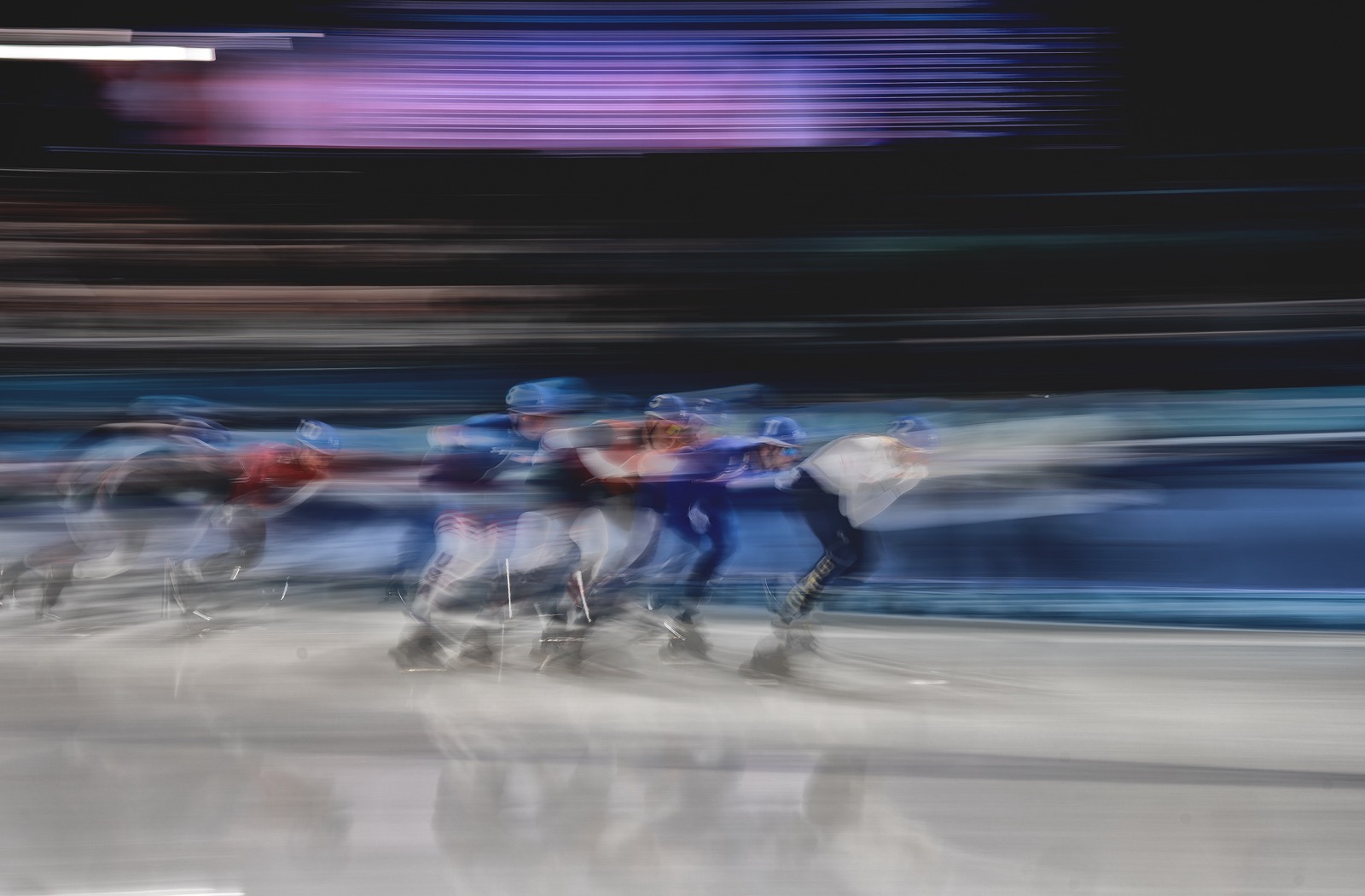 Short-track speed skaters rounding a bend, caught in motion blur.
